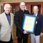 At a special luncheon at Southern Yacht Club, Pat White and Skip Hanemann present Fr. Raymond Fitzgerald, S.J. with a proclamation, naming him an honorary member of the Class of 1956.