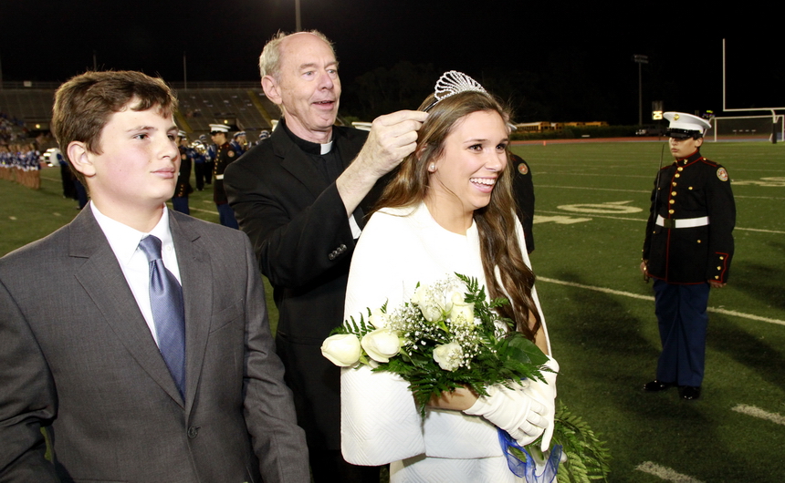 Fr. McGinn gingerly places the crown on Her Majesty, Sophie Millet, who is a senior at Mt. Carmel Academy. Her escort is freshman Christopher McMahon, who was standing in place of his older brother Michael, a fullback on the Blue Jay football team.