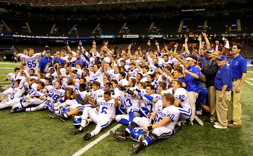 Displaying their state championship trophy, the 2014 Jesuit team faces a barrage of photographers on the field at the Mercedes-Benz Superdome. The Jays won the state title by defeating the John Curtis Patriots. 17-14.