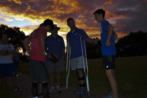 As the sun rises, Coach Rudy Horvath '86 (center on crutches) gives last-minute instructions to his runners prior to the Red, White, and Blue intrasquad scrimmage on August 27. Assistant Coach Ron Brignac is on Horvath's right.