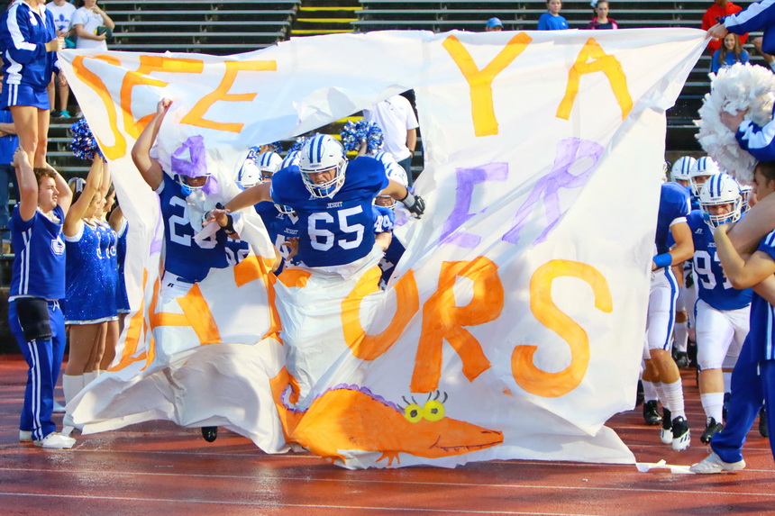 Connor Prouet (20) and Peyton Cox (65) burst through this week's football tapestry, the artistic work courtesy of the Jesuit Cheerleaders and Student Council.