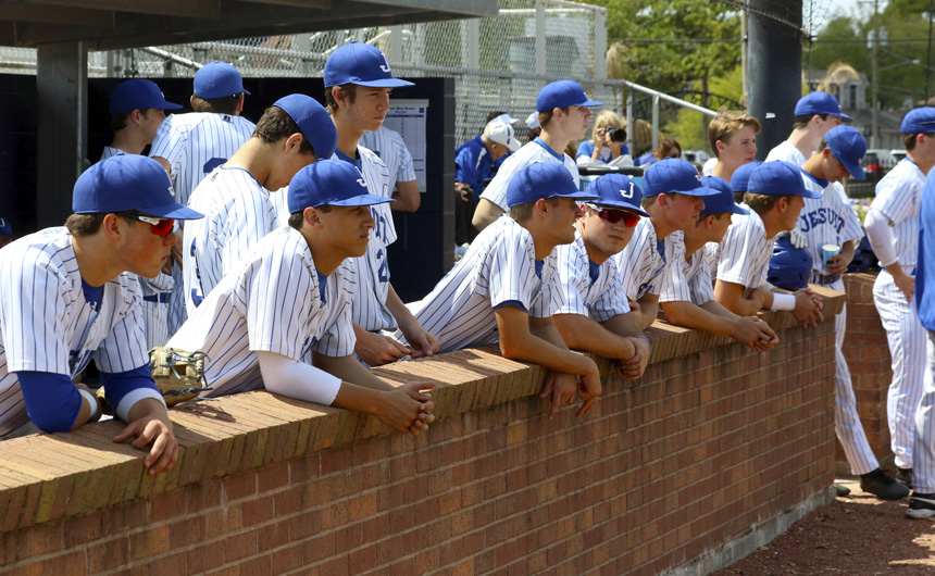 Jesuit players stand in the away dugout at Holy Cross's on-campus baseball field.
