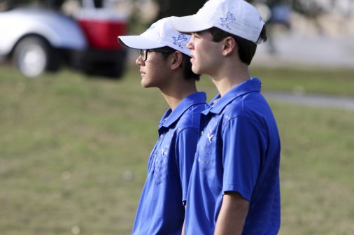Freshman Si Holmes and junior Jackson Maniscalco watch the final group finish the 9th hole at bayou oaks in City Park.